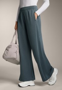 Široké nohavice z textúrovanej tmavomodrej látky s elastickým pásom a bočnými vreckami, v kombinácii s bielymi teniskami a svetlou kabelkou.