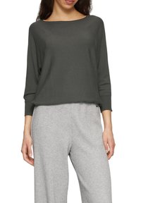 Dunkelgrüner, leichter Strickpullover mit weitem Halsausschnitt und drei Viertelärmeln, kombiniert mit grauen karierter weit geschnittenen Hosen.