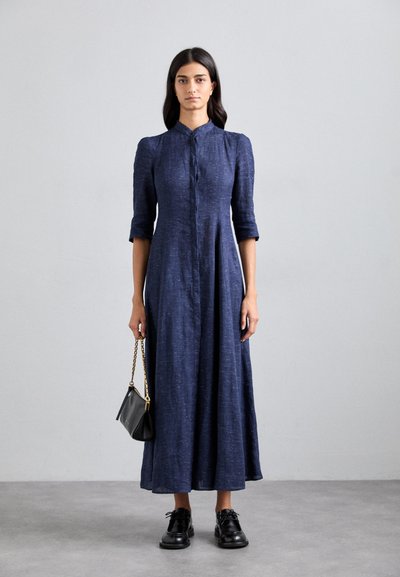 Navy blue long dress with a collar, button front, and three-quarter sleeves; paired with a small black handbag and black lace-up shoes.