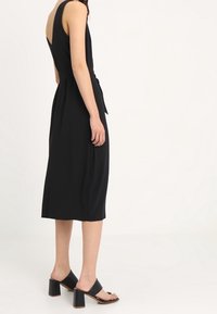 Musta ilmanhihaista mekkoa, jossa on tiukka yläosa ja leveä midi-hame, vyötäröllä solmu. Yhdistetty mustiin paksukorkoisiin sandaaleihin.