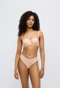 Lysebeige undertøysett med en glatt, formet BH med en subtil sløyfedetalj og matchende høytaljede truser, begge med sømløst design.