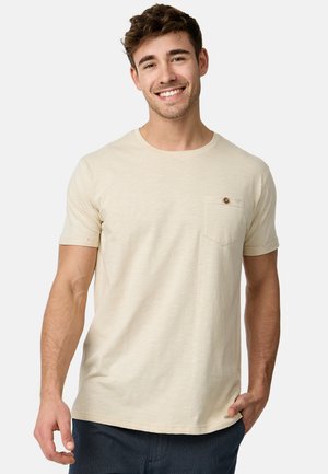 Camiseta de manga corta color beige claro, fabricada en un tejido suave, con un cuello redondo y un bolsillo en el pecho que cuenta con un botón decorativo.