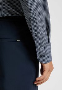 Marineblauwe shirt met een geometrisch patroon, met knoopmanchetten en een soepele textuur. Een BOSS-logo is zichtbaar op de donkere broek.
