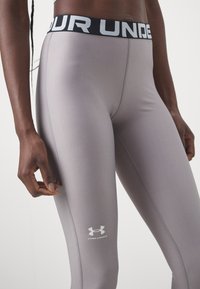 Under Armour leggings i ljusgrått tyg, med en svart midja som har vit text och logotyp, slät textur och tight passform.