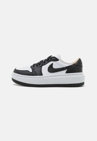 Baskets basses Nike noires et blanches avec logo swoosh noir, lacets noirs et semelle épaisse blanche sur fond gris clair uni.