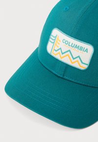 Tyrkysová baseballová čiapka z jednofarebnej látky, ktorá má obdĺžnikový biely nášivku s logom "Columbia Sportswear Co." a farebnými geometrickými akcentmi.