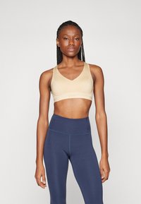 Sujetador deportivo beige con un diseño de escote en V, tirantes gruesos y una textura suave. Combinado con leggings azul marino de cintura alta con costuras azules.