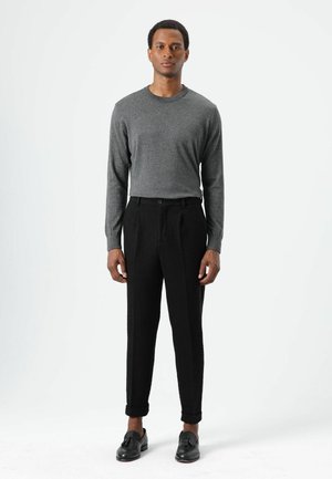 Grijs shirt met lange mouwen en een ronde hals, gecombineerd met zwarte taps toelopende broek met een gestructureerd patroon. Zwarte loafers maken de outfit compleet.