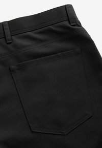 Black fabric pants with a smooth texture, featuring a single back pocket and belt loops, showcasing a clean, minimal design.