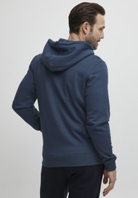 Sweatshirt bleu marine en tissu doux, avec une poche kangourou et une coupe décontractée. Le sweatshirt est doté d'un cordon de serrage et de poignets côtelés.