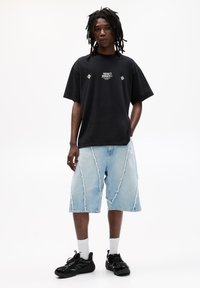 Sort bomuld t-shirt med hvide grafikker, kombineret med lyseblå slidte denim shorts med syninger. Sorte sneakers og hvide sokker.