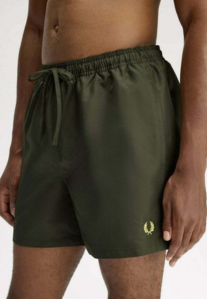 Pantaloncini da bagno verde scuro con elastico in vita e coulisse, indossati da un uomo senza maglietta, che mostrano un piccolo logo giallo a forma di alloro sulla gamba sinistra.