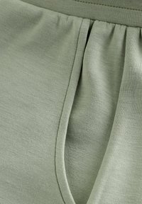 Tissu vert clair doux montrant un gros plan sur une couture avec des fronces et un détail de pli vertical.