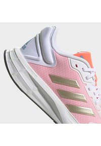 Scarpa da ginnastica rosa chiaro con tomaia in rete, dettagli bianchi e dorati, suola testurizzata, collo imbottito e dettaglio distintivo del logo.