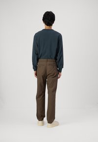 Dark blue long-sleeved top paired with brown elastic-waist pants, featuring two back pockets. Worn with light-colored sneakers.