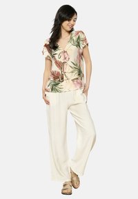 Blusa floreale in rosa chiaro e crema, con maniche corte a sbuffo e scollatura a V con dettaglio a fiocco. Abbinata a pantaloni larghi color crema.