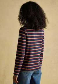 Tumestriibuline pikkade varrukatega T-särk tumesinisest kangast roosa ja beeži triibuga, ümaramas kaelas ja logopatchiga varruka peal. Vabaaja lõige.