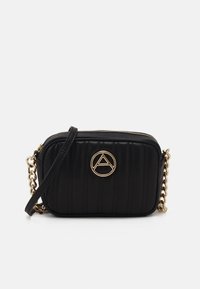 Borsa a tracolla trapuntata nera con logo circolare dorato, tracolla a catena e chiusura con zip. Presenta cuciture verticali per aggiungere texture.