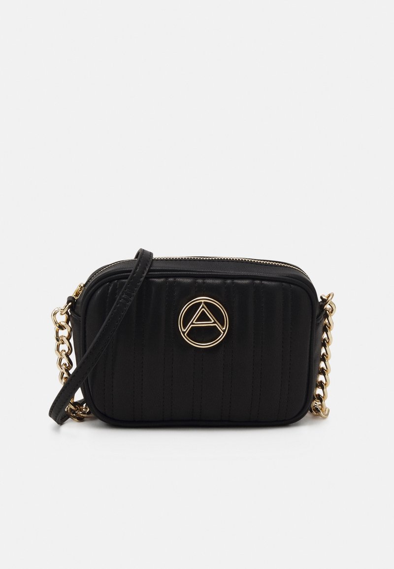 Borsa a tracolla trapuntata nera con logo circolare dorato, tracolla a catena e chiusura con zip. Presenta cuciture verticali per aggiungere texture.