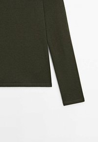 Chemise en tricot vert olive à manches longues avec une fente latérale, présentée sur un fond blanc, montrant les détails des manches et de l'ourlet inférieur.