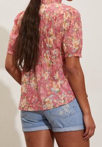 Floral pink blouse with short puffed sleeves, gathered back detail, paired with light blue denim shorts featuring embroidered accents.