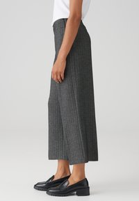 Grijze, wijde broek met een subtiele houndstooth-patroon, gemaakt van textuurstof. Gecombineerd met zwarte loafers, wat een slanke silhouet toont.