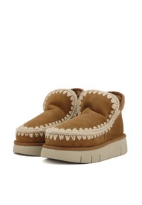 Bruine suède instappers met een gewatteerde kraag, decoratieve witte stiksels en een gestructureerde beige platformzool.