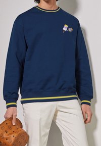 Sweat-shirt marine avec col et poignets côtelés accentués de jaune. Présente une broderie ludique de glace sur la poitrine. Texture de tissu lisse.