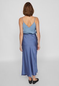 Robe en satin bleu avec un dos en V. La jupe est longueur cheville avec une texture lisse. Associée à des ballerines noires.