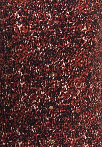 Tissu à motifs rouge et noir avec des accents blancs, présentant une fermeture avant à boutons et des boutons métalliques, texture lisse, design moderne.
