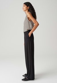 Leichtes, gestreiftes Tanktop mit weiten Armöffnungen, kombiniert mit hoch taillierten schwarzen Hosen und flachen schwarzen Schuhen mit Schleifen. Glatte Texturen.