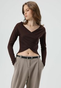 Bruine geribbelde top met lange mouwen en wikkelontwerp, gecombineerd met beige broek met hoge taille en een zwarte riem. Minimalistisch en nauwsluitend.