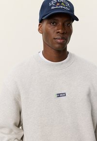 Άνδρας που φορά σκούφο "Les Deux" σε ναυτικό μπλε και ανοιχτογκρι φούτερ με μικρό λογότυπο "Les Deux" στο στήθος, ουδέτερο φόντο.