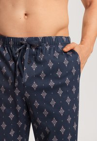 Navyblauwe geweven broek met een bloemig ruitpatroon in roze en wit, elastische tailleband met koord, zijzakken en knoopdetails.