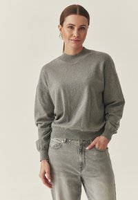 Pull gris léger avec un col rond, des poignets et un ourlet côtelés. Assorti à un jean denim gris clair, avec un style classique à cinq poches.