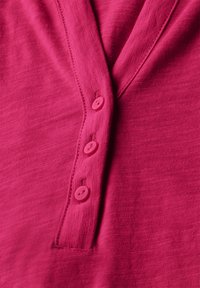 Fuchsiová bavlněná košile s výstřihem do V, čtyřmi ladícími knoflíky a texturovanou tkaninou s jemným vzorem.