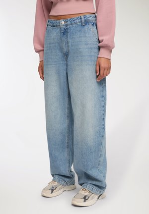 Jeans a vita alta di un blu chiaro, a gamba larga, realizzati in denim, con chiusura a bottoni e due tasche laterali, abbinati a sneaker neutre.