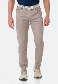 Hellgraue, strukturierte Hose im Slim-Fit-Design, mit einem weißen Gürtel mit silbernen Nieten und Fronttaschen. Tragen mit beigen Schuhen.