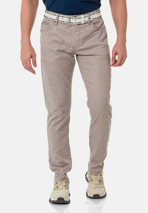 Hellgraue, strukturierte Hose im Slim-Fit-Design, mit einem weißen Gürtel mit silbernen Nieten und Fronttaschen. Tragen mit beigen Schuhen.