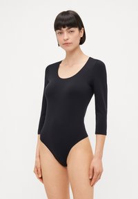 Bodysuit noir à manches longues avec un décolleté en coeur, fabriqué à partir d'un tissu lisse et extensible. A une silhouette ajustée et des jambes hautes.