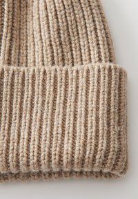 Beige gebreide muts met geribde textuur, gemaakt van zacht, dik garen en met een omgeslagen rand voor extra warmte en stijl.