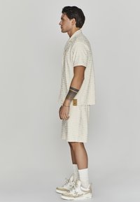 Lys beige kortærmet skjorte med geometrisk mønster parret med matchende shorts. Neutrale sneakers med cremede detaljer og hvide sokker.