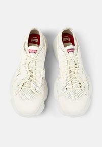 White athletic shoes with mesh detailing, round toes, and flat laces. Features a padded collar and a red label on the tongue. Textured sole.