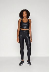 Černý sportovní komplet se skládá z krátkého topu a legín s vysokým pasem s lesklým, texturovaným designem ve vzoru leoparda.