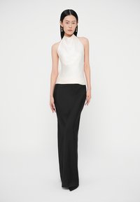 Ένα αμάνικο, ελεφαντόδοντου χρώματος τοπ halter συνδυασμένο με μια μαύρη, μακριά φούστα μέχρι το πάτωμα. Το τοπ έχει λεία υφή, ενώ η φούστα έχει κομψή εφαρμογή.