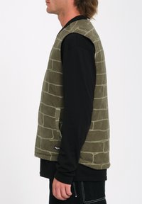 Grøn fleece vest med et struktureret mursten mønster og sidelommer, parret med en sort langærmet skjorte. Simpelt, udekoreret design.