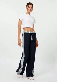 Navy Sweatpants mit hellblauen und weißen vertikalen Streifen, elastischem Bund mit Kordelzug, kombiniert mit einem kurzen weißen T-Shirt.