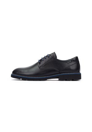 Zapatos de cuero negro con cordones presentan un acabado suave, acentos azules y una suela de goma gruesa con detalles de tracción. Costuras visibles a lo largo de los bordes.