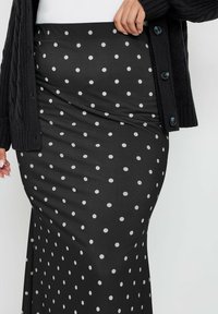 Musta pilkkupuku, jossa on muotoiltu siluetti, valmistettu sileästä kankaasta. Ominaisuuksiin kuuluu korkea vyötärö ja pieniä valkoisia ympyräkuvioita.