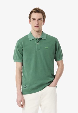 Grünes Polohemd aus strukturiertem Stoff, mit Kragen und kurzen Ärmeln. Mit einem kleinen gestickten Logo und einem Etikett am Saum.
